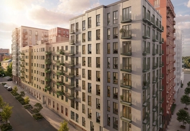 Moderna flervåningshus ligger längs en ren stadsgata under en delvis molnig himmel.