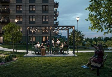 Pergola med utemöbler och människor. Bostadshus i bakgrunden.
