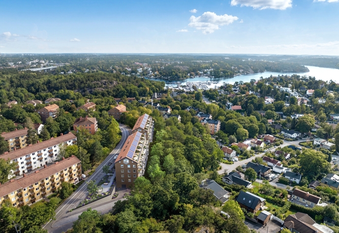Podium. Flygfoto över ett förortsområde med bostadshus, träd och en flod i bakgrunden under en blå himmel.