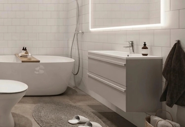 Modernt badrum med fristående badkar, väggmonterat handfat, bakgrundsbelyst spegel och handduk som hänger på väggen.