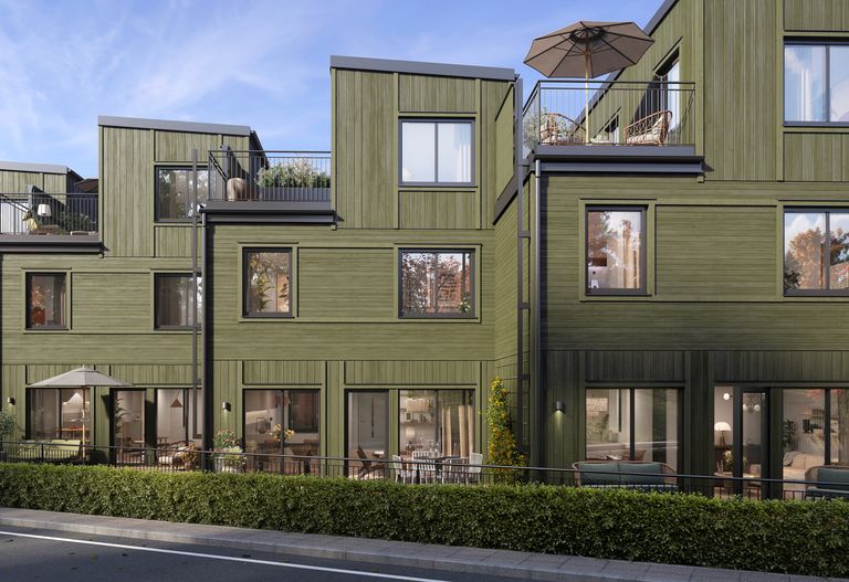 Gröna hus sett från gatan med häck och altaner i förgrunden