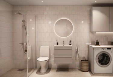 Vitt, modernt badrum med dusch, toalett, handfat, rund belyst spegel och komimaskin med överskåp.