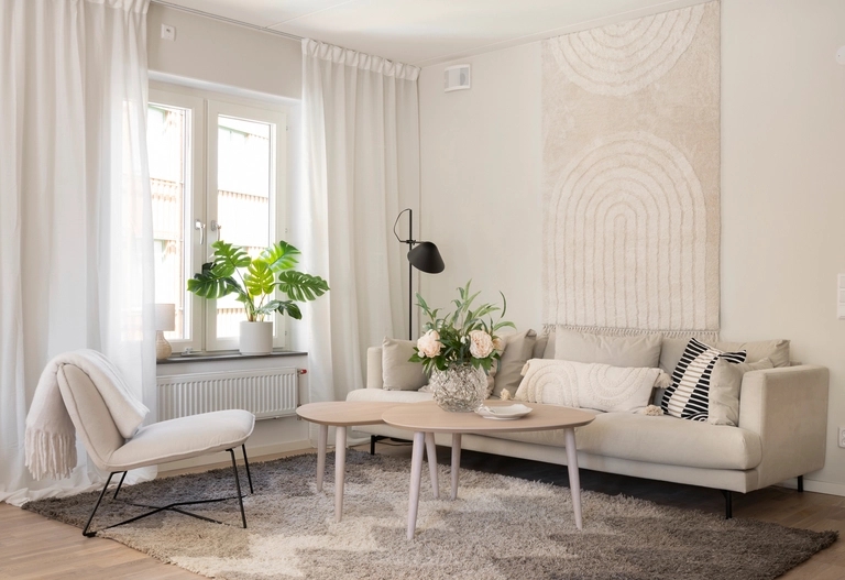 Vardagsrum i neutral ton med en beige soffa, modern inredning, krukväxter och en stor abstrakt väggbonad.