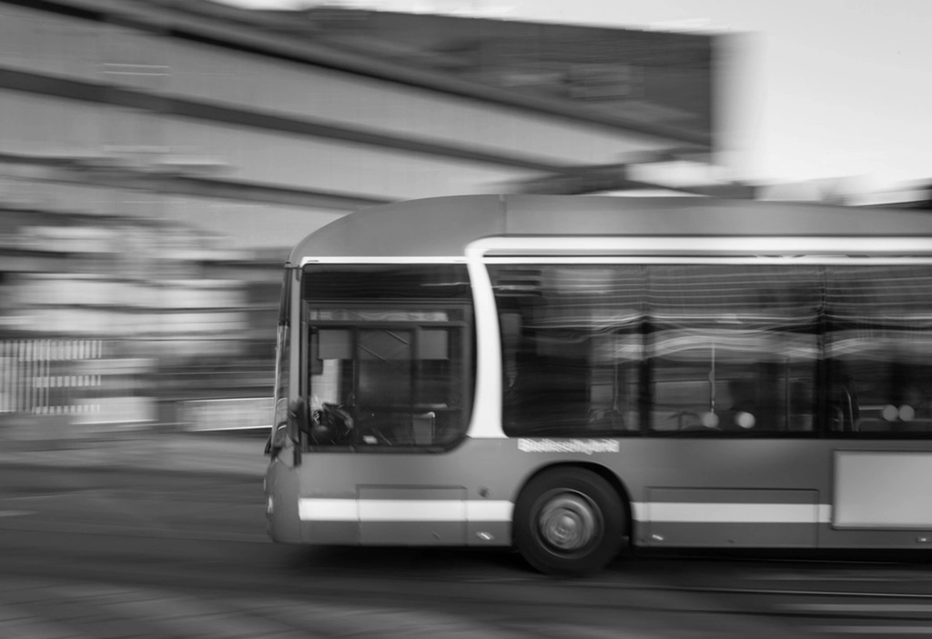 En stadsbuss i rörelse passerar en suddig urban bakgrund i svartvitt.