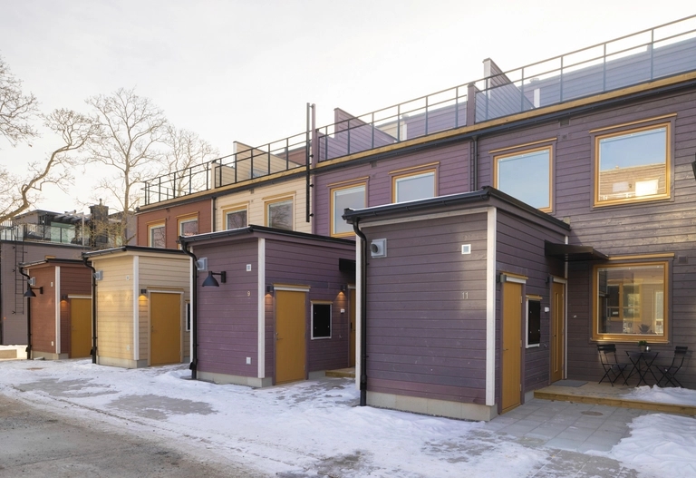 Rad av moderna radhus i tre våningar med entréer, platta tak och snö på marken.