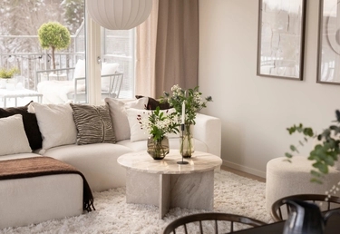 Modernt vardagsrum med vit soffa, runt soffbord i marmor och stora fönster med utsikt över en snöig terrass.