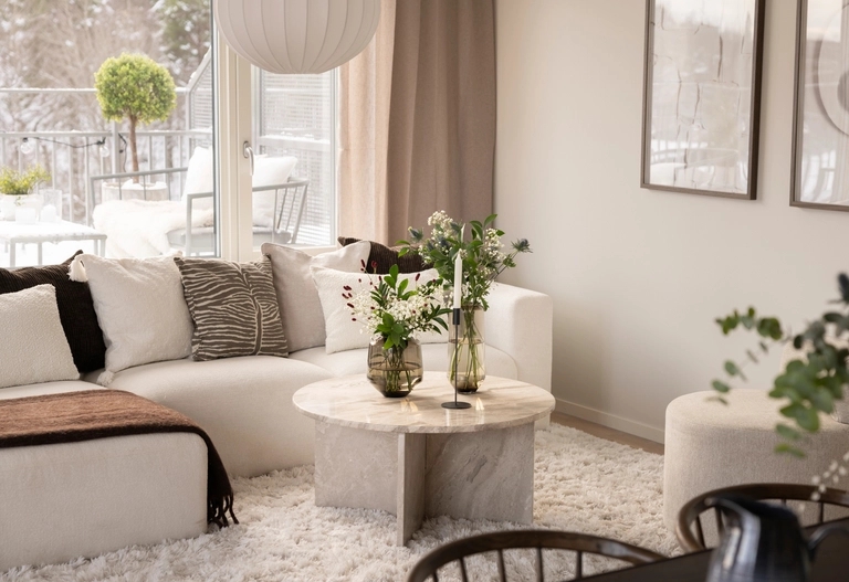 Modernt vardagsrum med vit soffa, runt soffbord i marmor och stora fönster med utsikt över en snöig terrass.