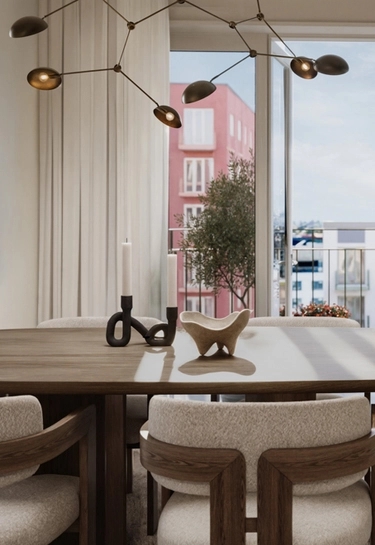 Matbord i trä med ljusstake och skulptur under designlampa. Utanför fönstret syns en rosa byggnad.