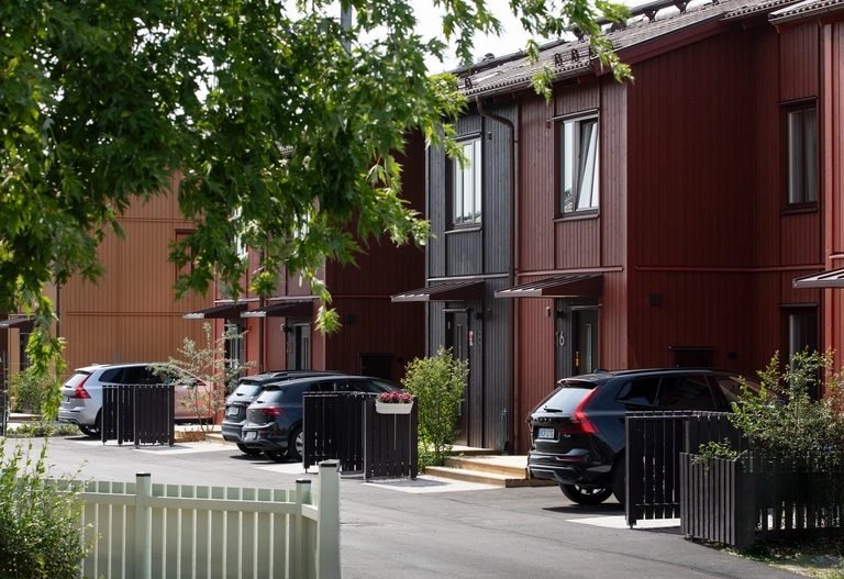 Gata med röda och svarta radhus, egen parkering och svarta trästaket för soptunnor.