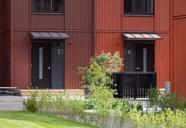 Två entréer med svarta dörrar och skärmtak på röd träfasad, plantering framför.