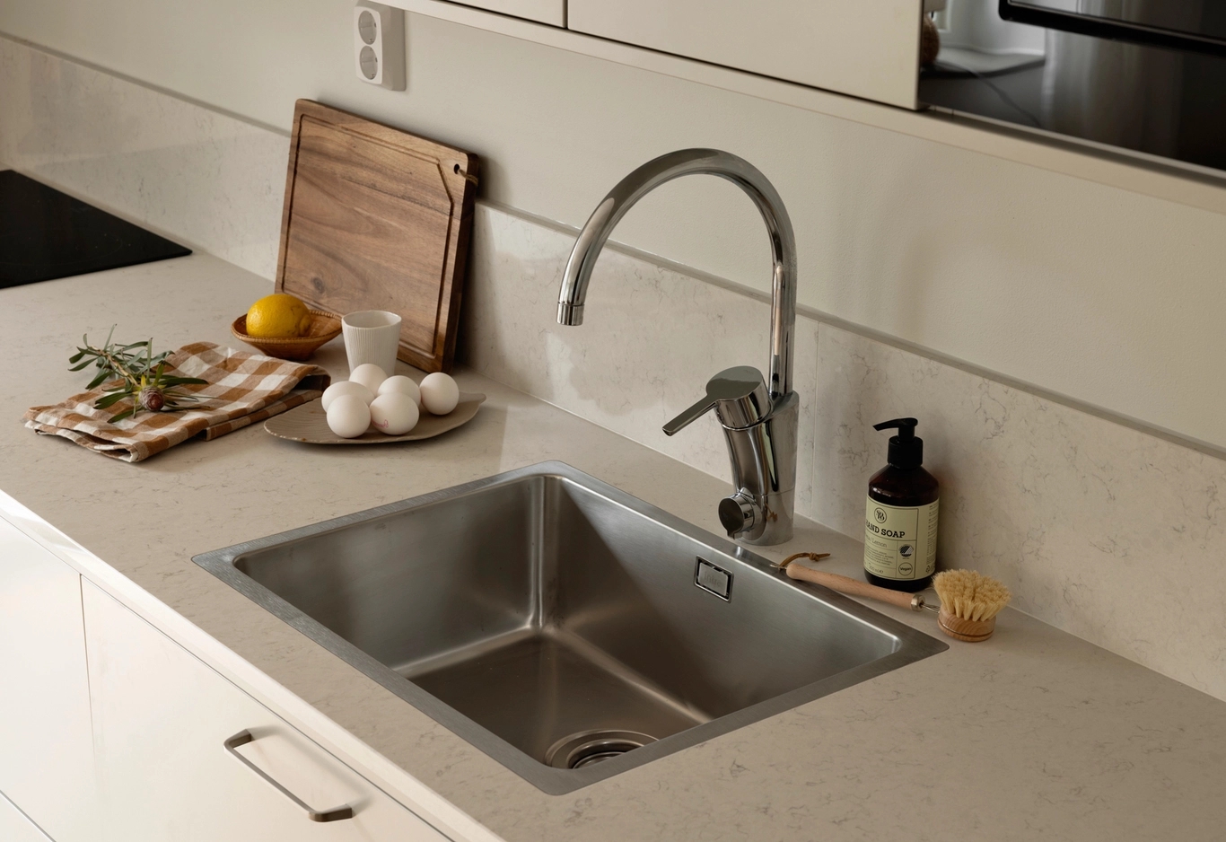 En modern diskbänk med kran, tvålpump och bänkskivor med bland annat ägg, citron och en skärbräda.