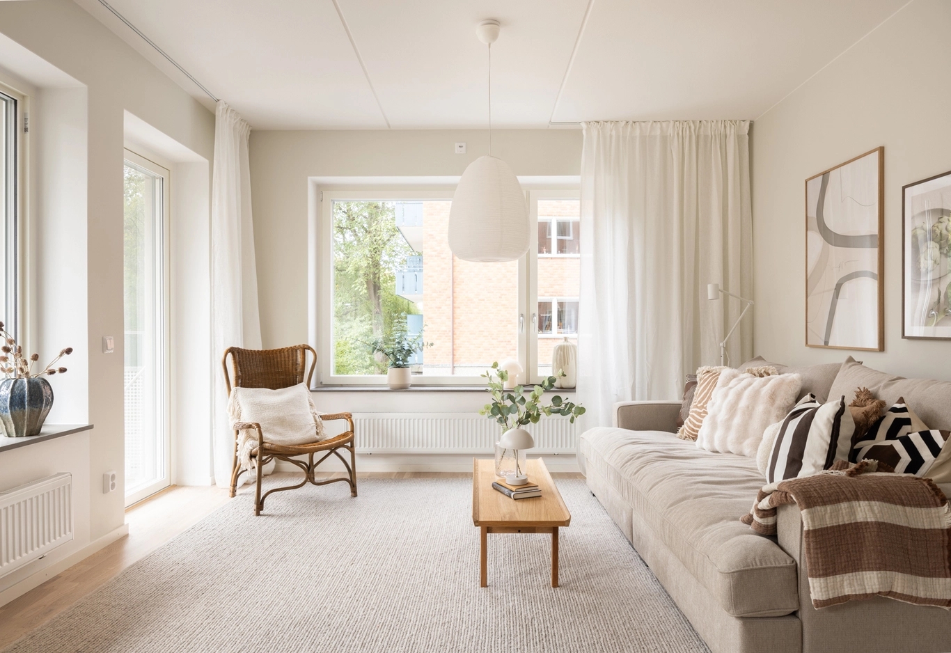 En terrass med trämöbler, inklusive ett runt bord, korgstolar och en mysig sittgrupp med en soffa, kuddar och en matta. Växter och grönska pryder utrymmet.