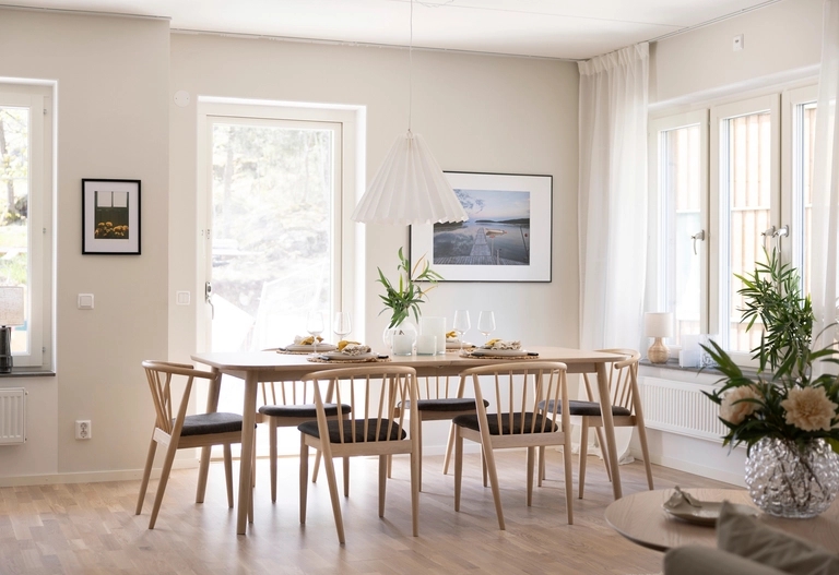 Öppen planlösning med matsalsbord, sex stolar och minimalistisk inredning nära stora fönster som släpper in naturligt ljus.