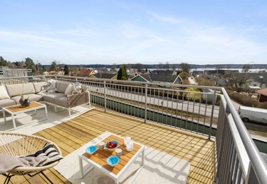 En takterrass med soffgrupp som har utsikt över ett bostadsområde och fjärran vatten under klar himmel.