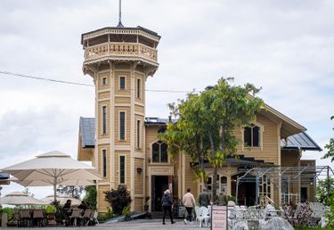 Gul träbyggnad med ett torn, uteservering med cafébord, konditori Lyran