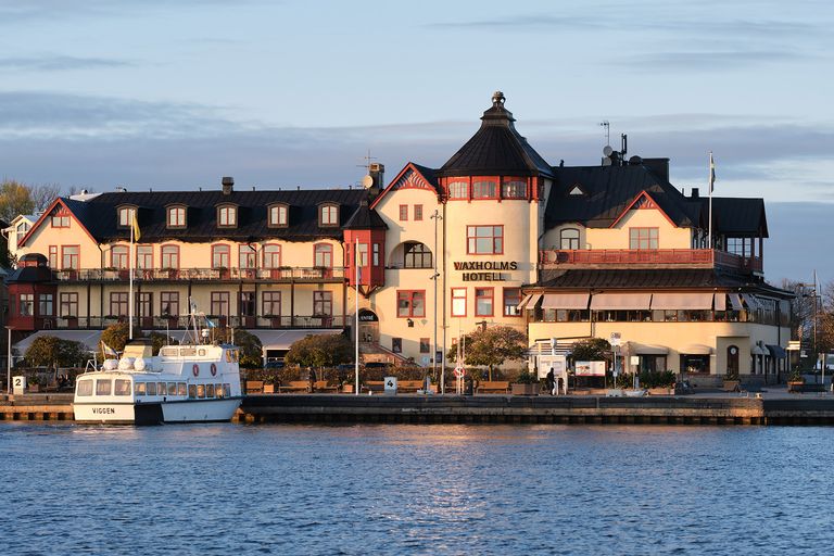 En karusell av metall för lekplatser står på gräs omgiven av höstträd med gula och orange löv.