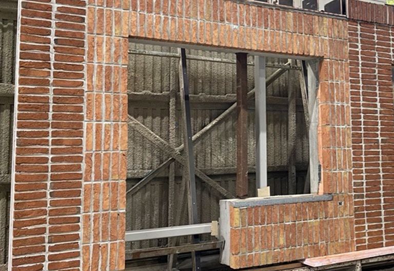 En delvis konstruerad tegelvägg med ofullbordad fönsterkarm. Metallstöd syns bakom väggen.