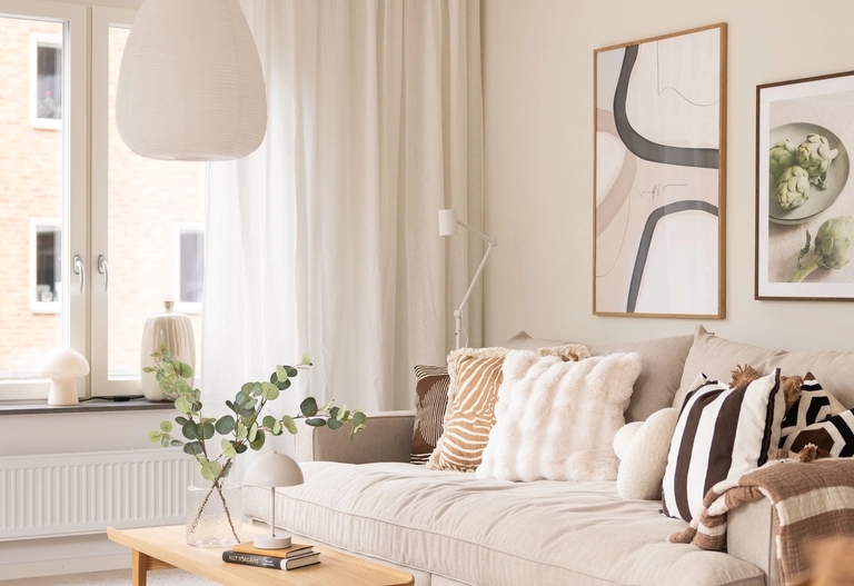 Modernt vardagsrum med en beige soffa, dekorativa kuddar, ett soffbord i trä och minimalistisk väggkonst.