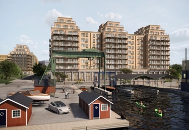 Moderna lägenhetsbyggnader vid en kanal med röda båthus, en grön lyftkran, kajaker och människor.