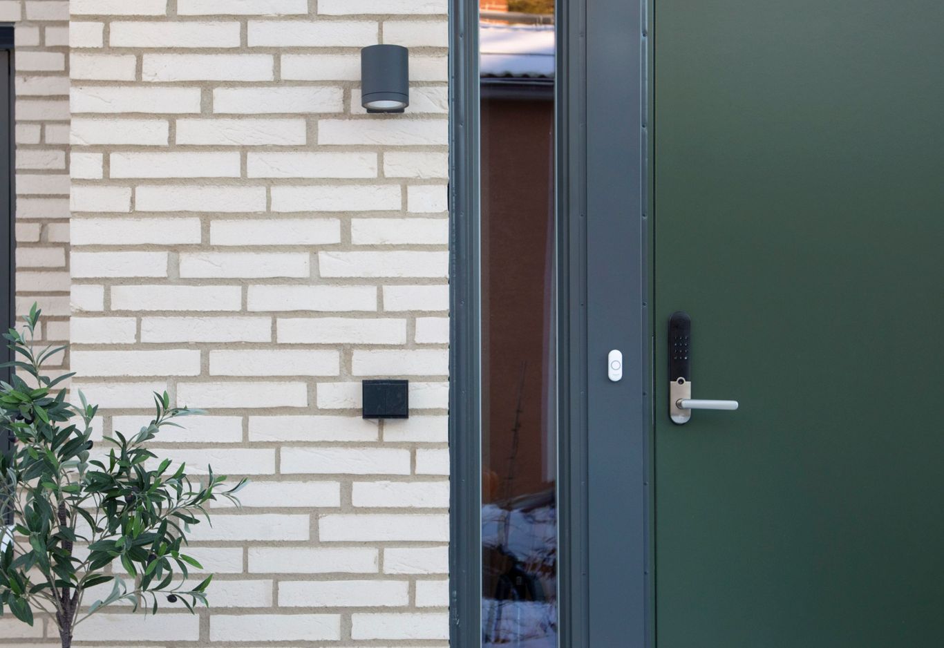 En grön dörr med ett silverhandtag och elektronisk knappsats vid handtaget. En liten buske till vänster.