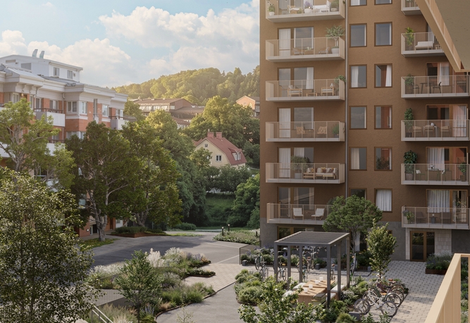 Modernt brunt flerbostadshus med balkonger, en lummig innergård och andra byggnader omgivna av träd under solig himmel.