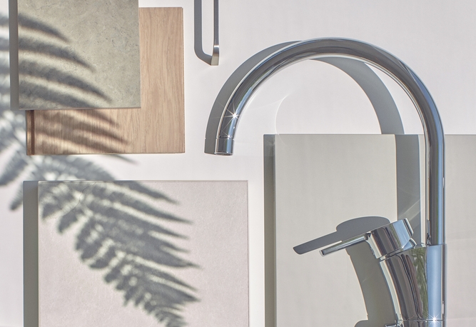 Moodboard över materialval i en nyproducerad bostad. En modern kran i krom tillsammans med rektangulära prover och en skugga av ett ormbunksblad mot en vit bakgrund.