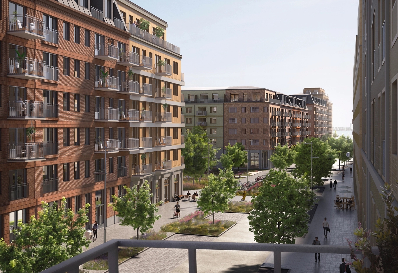 Rödbruna tegelbyggnader med balkonger omger ett soligt, grönskande torg med gående människor i ett nybyggt stadskvarter.