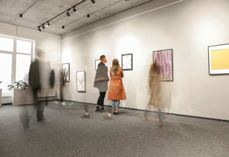 Besökare som tittar på konstverk i ett galleri med några i rörelse, vilket skapar en suddig effekt.