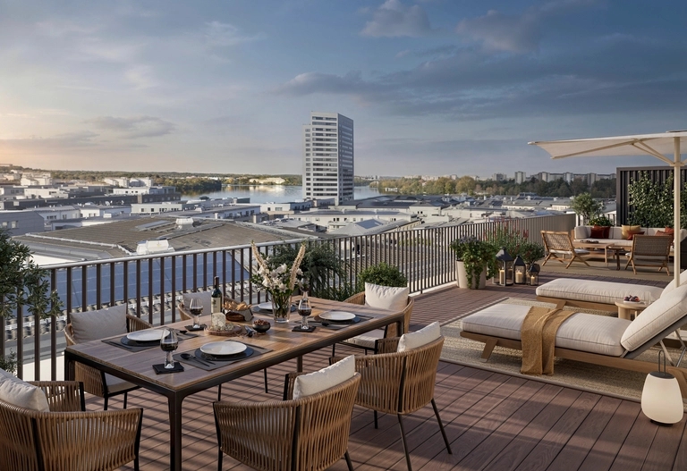 En takterrass med ett matbord, solstolar och stadens byggnader i bakgrunden i solnedgången.