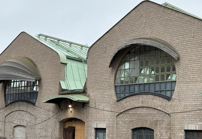 Tegelbyggnad med stora, rundade fönster och gröna takpartier i plåt, fotograferad en mulen dag.