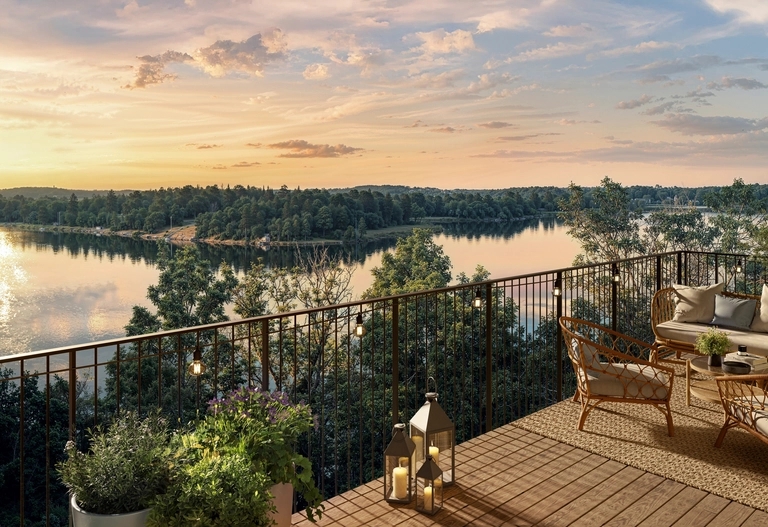 En balkong med uteservering har utsikt över en sjö och skog under en färgstark solnedgångshimmel.