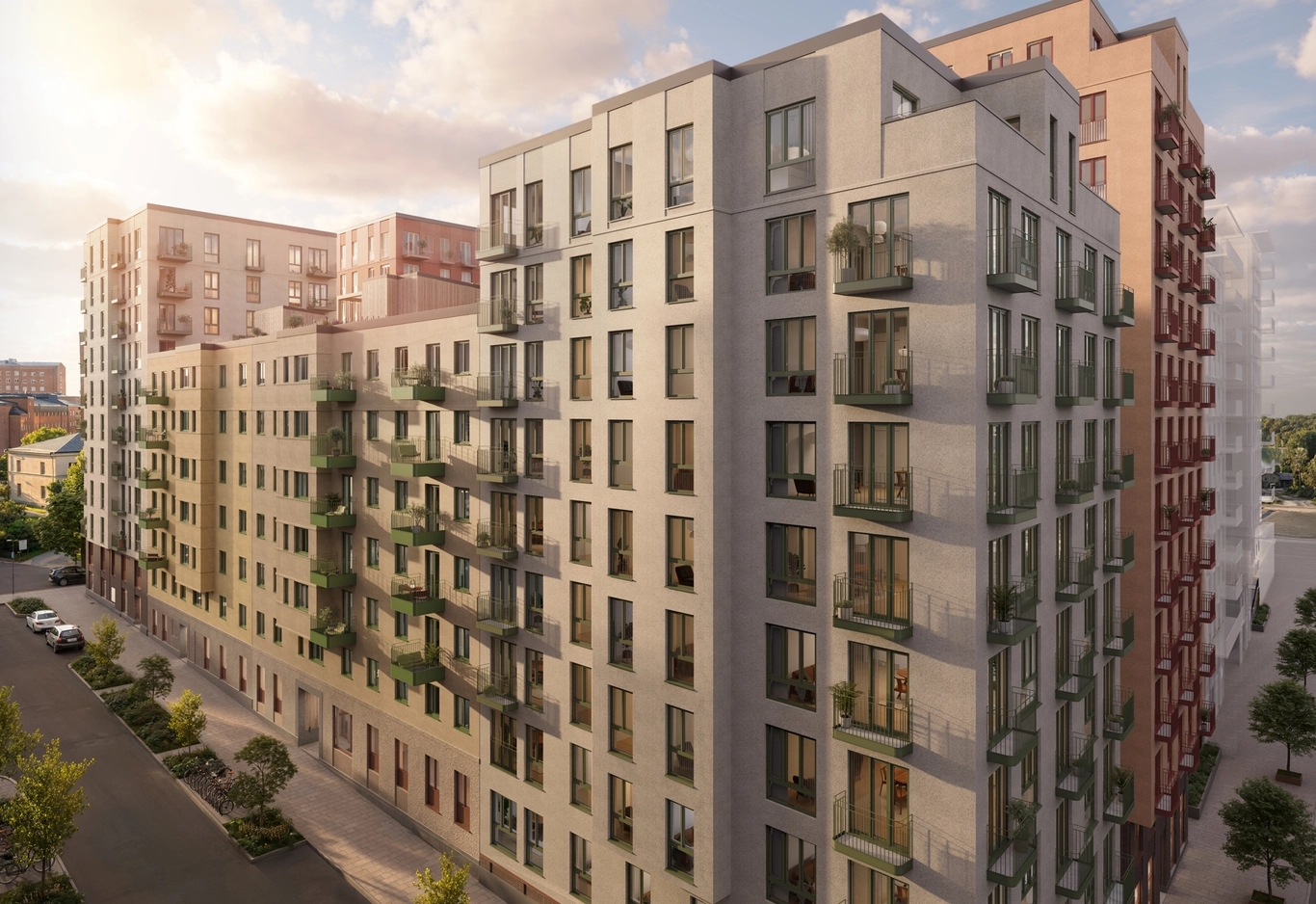 Moderna flerbostadshus med ljusa och persikofärgade fasader, balkonger och träd längs en gata i varmt kvällsljus.