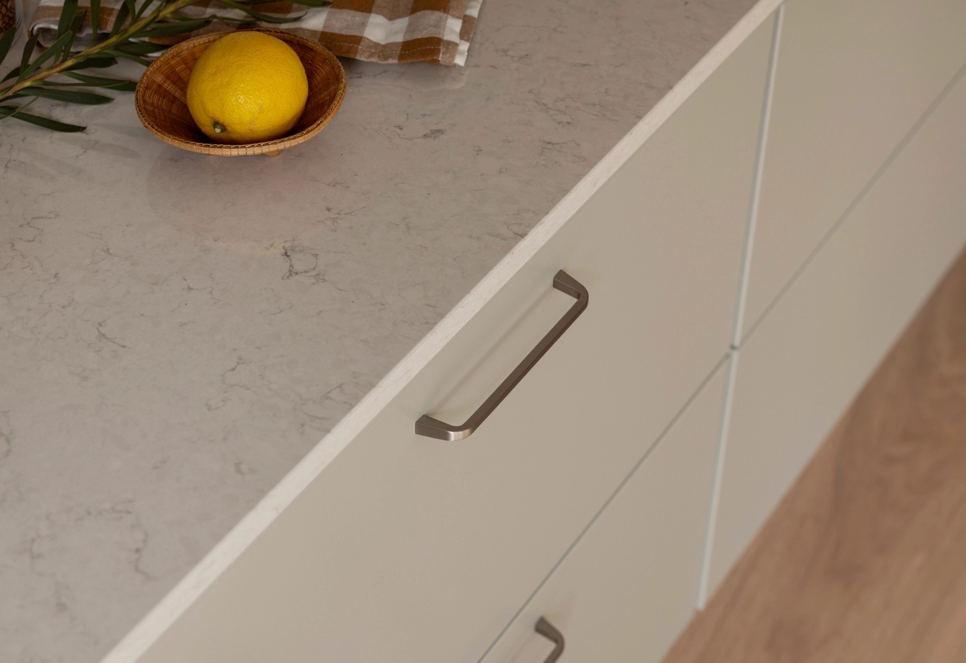 Ljusa kökslådor med metallhandtag, en bänkskiva, en citron i en träskål och en rutig trasa.