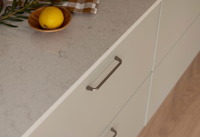 Ljusa kökslådor med metallhandtag, en bänkskiva, en citron i en träskål och en rutig trasa.