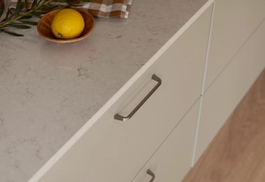 Ljusa kökslådor med metallhandtag, en bänkskiva, en citron i en träskål och en rutig trasa.