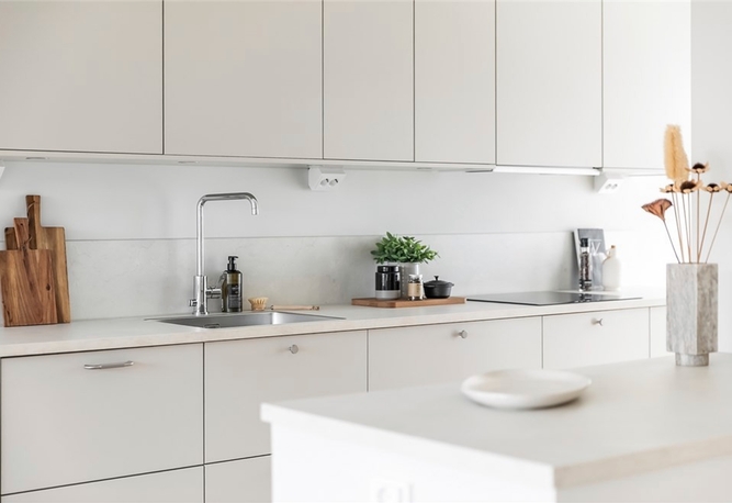 Ett modernt kök med vita skåp, diskbänk, krukväxter, skärbrädor och minimal bänkinredning.
