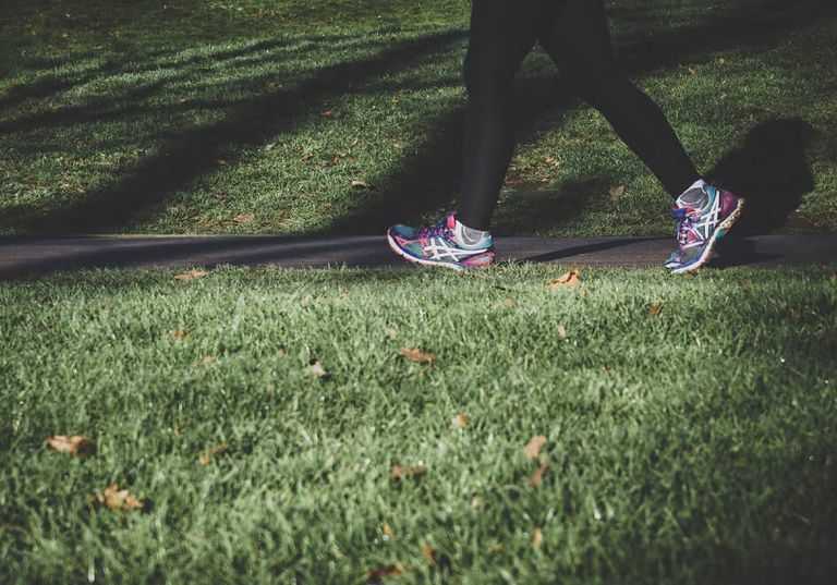 Person i svarta leggings och färgglada sneakers går på en asfalterad stig bredvid gräs i en park.
