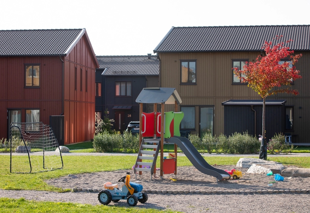 Lekplats med rutschkana och sandlåda på gården, framför radhus i rött, svart och olivgrönt trä