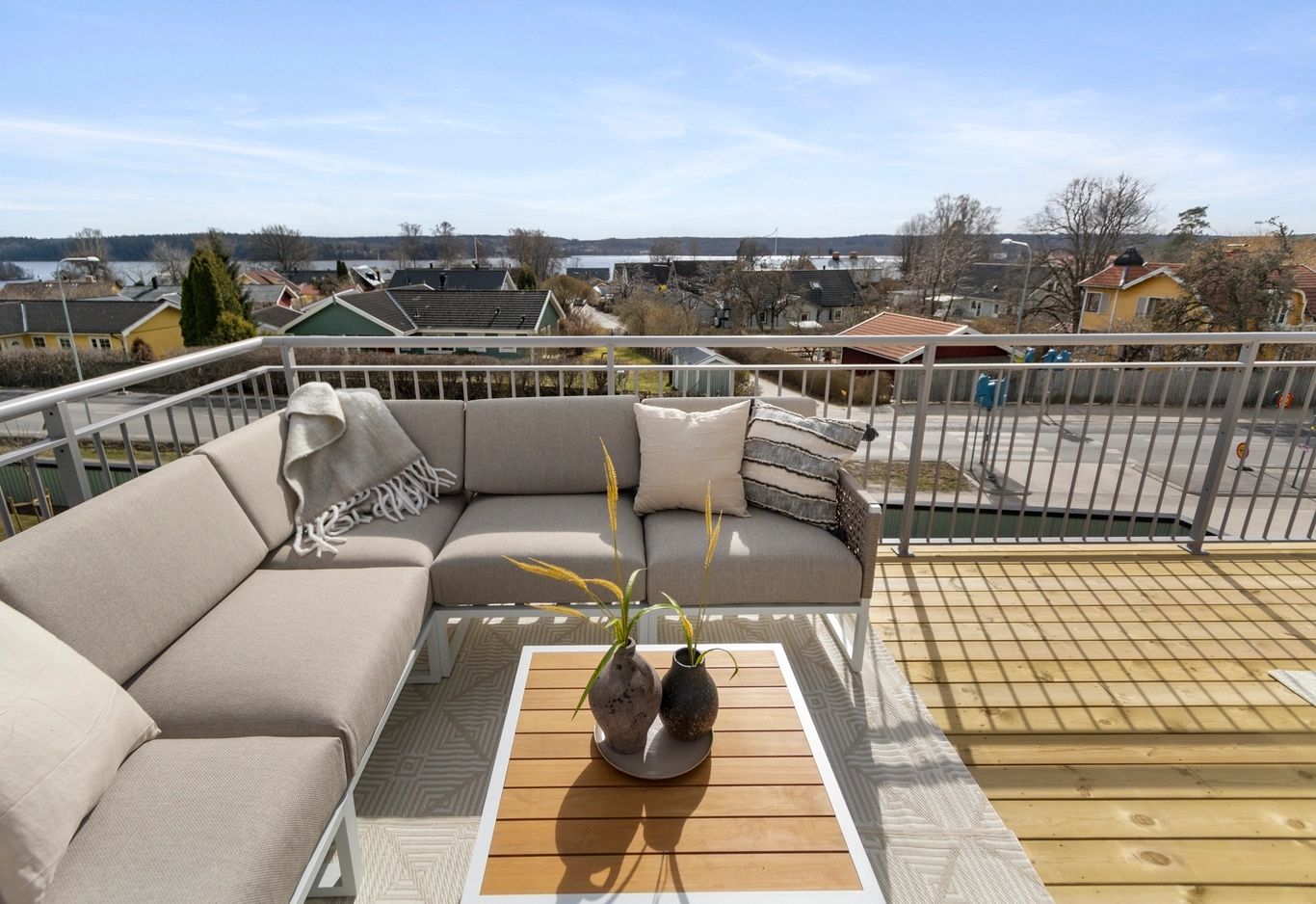 Takterrass med en beige soffa, dekorativa kuddar och ett soffbord i trä med utsikt över ett bostadsområde.