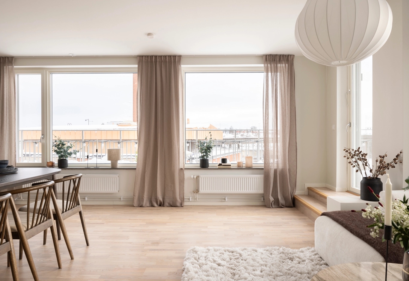 Ljust, modernt vardagsrum och matplats med stora fönster, ljusa trägolv och minimalistisk inredning.