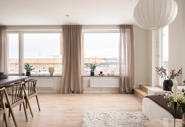 Ljust, modernt vardagsrum och matplats med stora fönster, ljusa trägolv och minimalistisk inredning.
