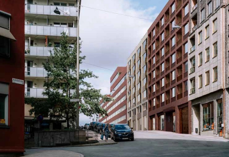 Ett bostadshus klätt i tegelfasad syns längs med en trafikerad stadsgata.