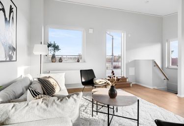 Minimalistiskt vardagsrum med vit soffa, svart stol och runt soffbord på en vit matta.