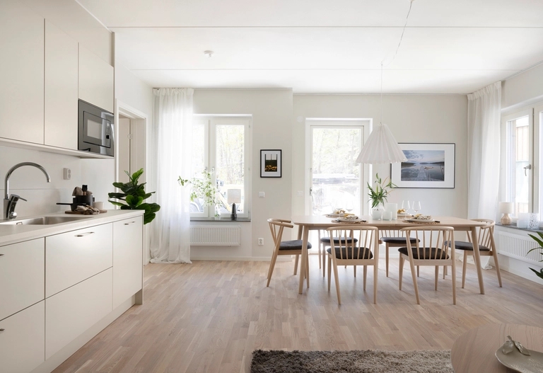 Modernt, minimalistiskt kök och matplats med ljusa trägolv, neutrala möbler och naturligt ljus från stora fönster.