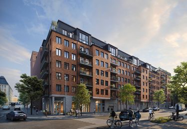 Flerfamiljshus med tegelfasad på ett gathörn med människor som går och cyklar, och bilar parkerade längs vägen.