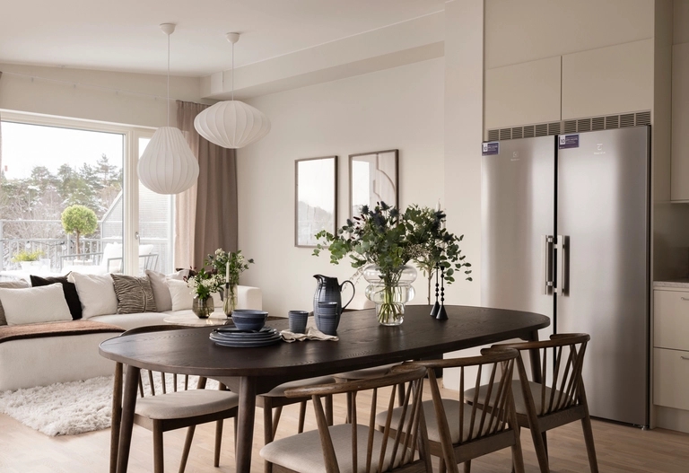 Modern matplats med bord och stolar i mörkt trä och modern inredning intill ett ljust vardagsrum och kök.