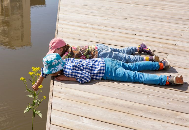 Två barn som ligger på en brygga och tittar på vattnet nedanför