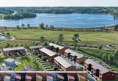 Flygfoto över Sjöstråkets kvarter, gröna gräsmattor och en slingrande väg nära en stor sjö och skogsområde i bakgrunden.